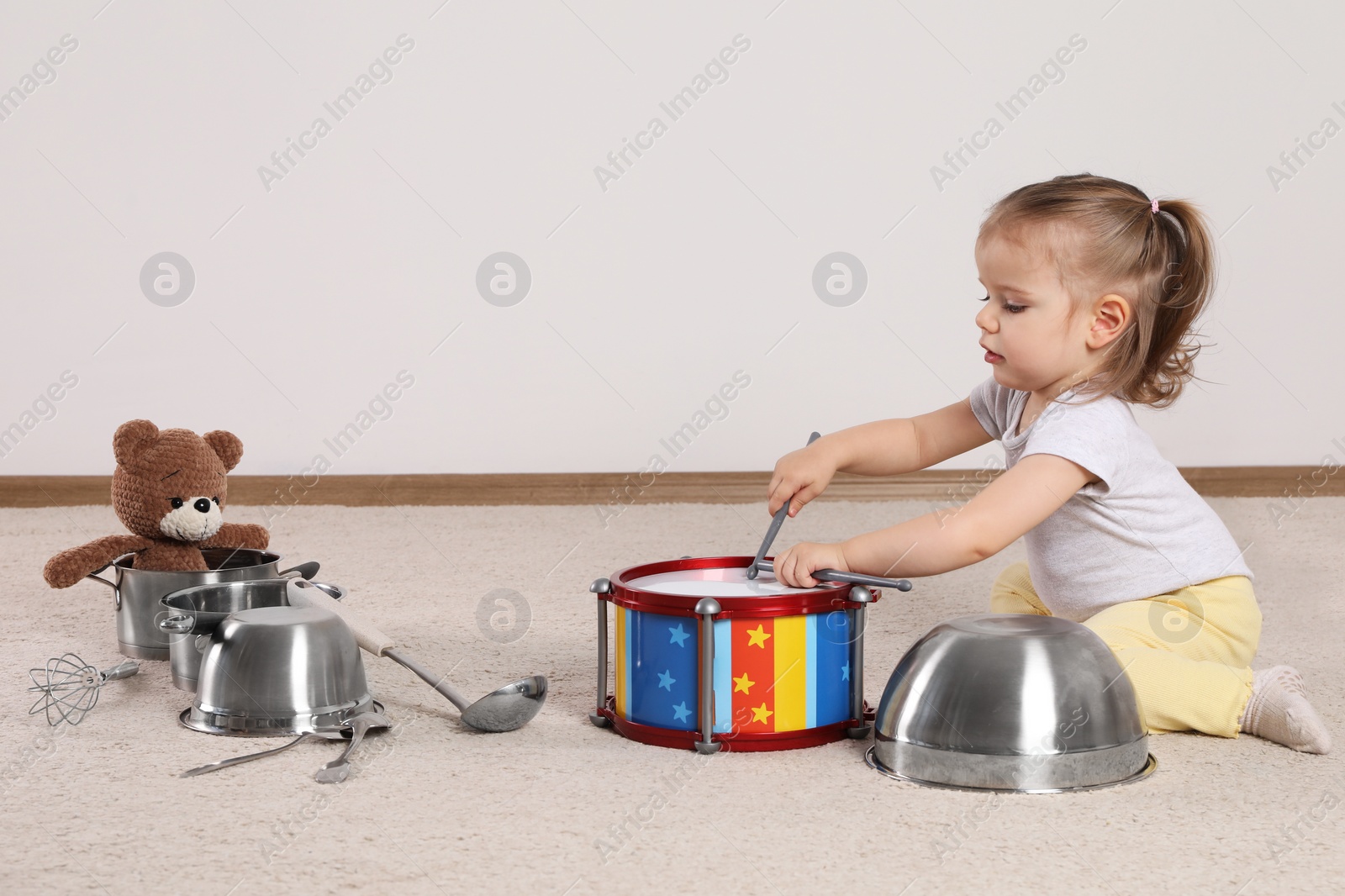 Photo of Cute little girl with cookware and toy drum at home