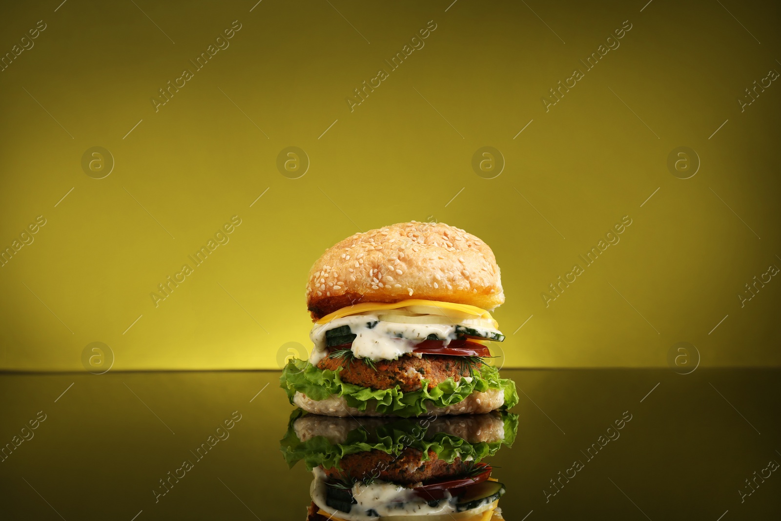 Photo of Delicious vegetarian burger on mirror surface against olive background