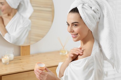 Photo of Beautiful happy woman in stylish bathrobe applying cream on shoulder in bathroom