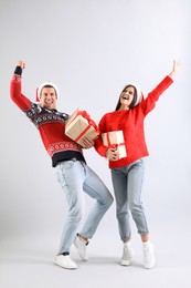 Photo of Beautiful happy couple in Santa hats with Christmas gifts having fun on light background