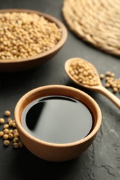 Photo of Tasty soy sauce in bowl and soybeans on black table, closeup