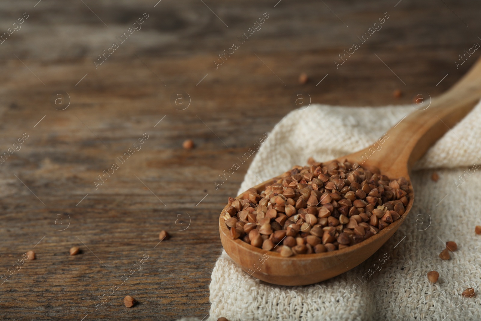 Photo of Spoon with uncooked buckwheat on wooden table. Space for text