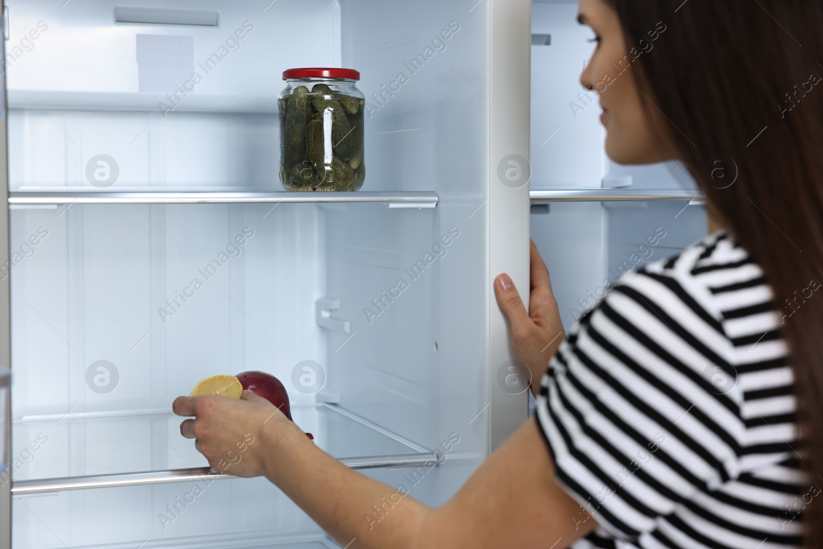 Photo of Young woman taking lemon out of empty refrigerator, selective focus