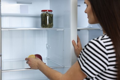 Young woman taking lemon out of empty refrigerator, selective focus