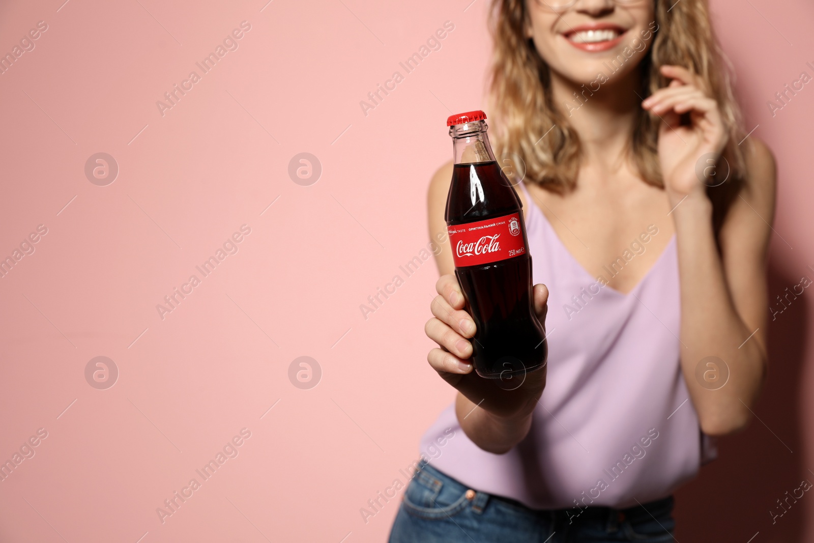 Photo of MYKOLAIV, UKRAINE - NOVEMBER 28, 2018: Young woman with bottle of Coca-Cola on color background, space for text