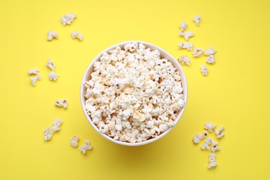 Photo of Paper bucket with delicious popcorn on yellow background, flat lay