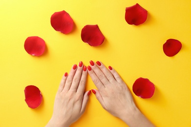 Woman holding hands near rose petals on color background, top view. Beautiful nail polish