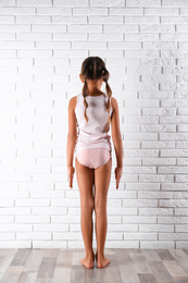 Photo of Little girl in underwear near white brick wall, back view