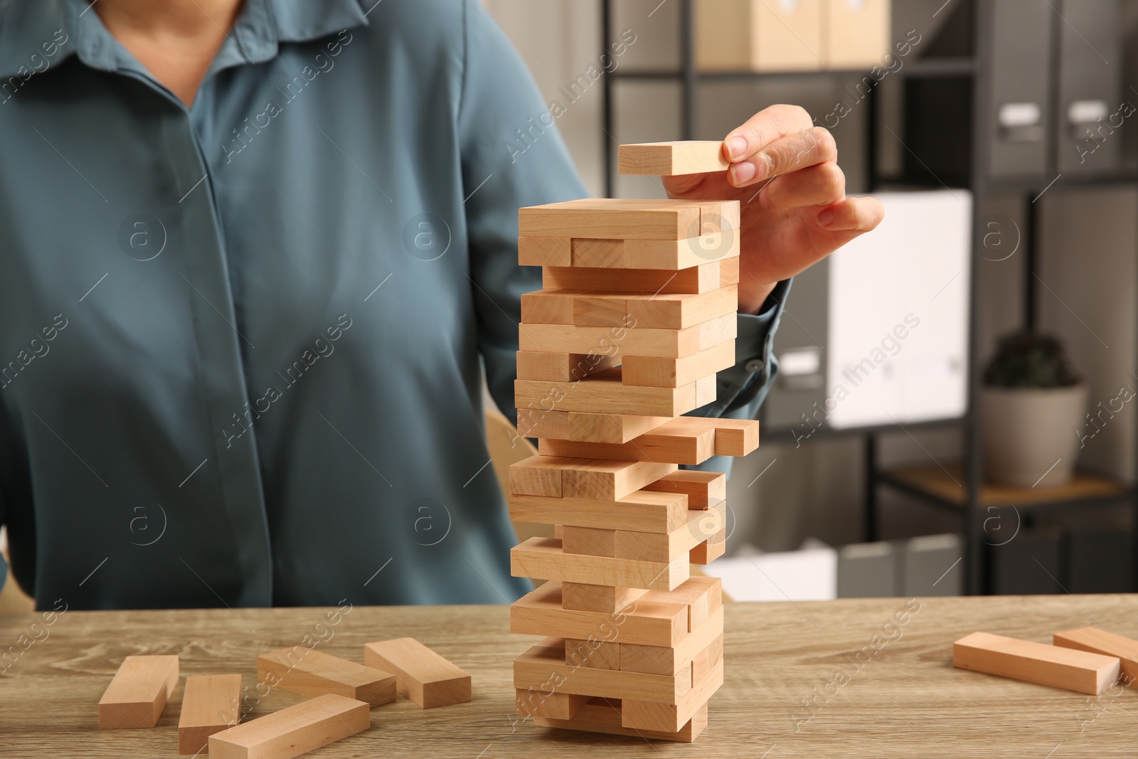 Photo of Playing Jenga. Woman building tower with blocks at wooden table indoors, closeup