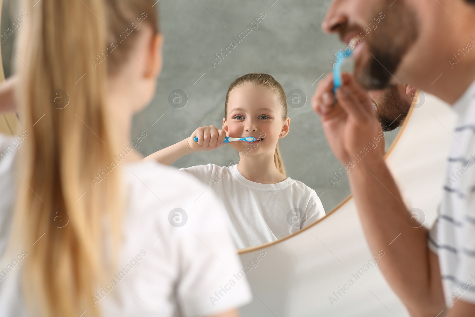 Photo of Father and his daughter brushing teeth together near mirror indoors