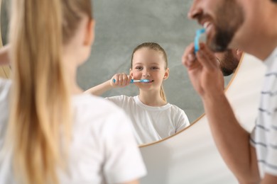 Photo of Father and his daughter brushing teeth together near mirror indoors