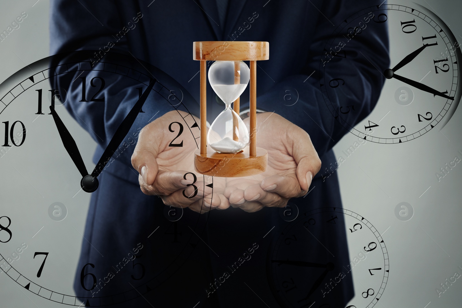 Image of Time management concept. Man with hourglass surrounded by clocks, closeup