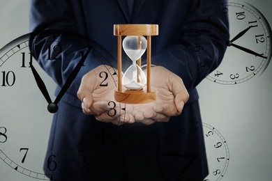 Time management concept. Man with hourglass surrounded by clocks, closeup
