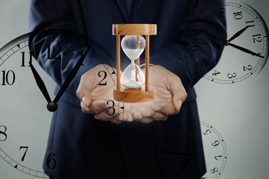 Image of Time management concept. Man with hourglass surrounded by clocks, closeup