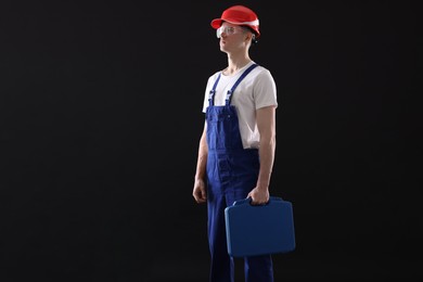 Professional repairman with tool box on black background. Space for text