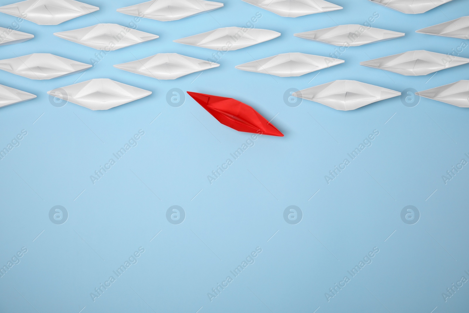 Photo of Red paper boat floating away from others on light blue background, flat lay with space for text. Uniqueness concept