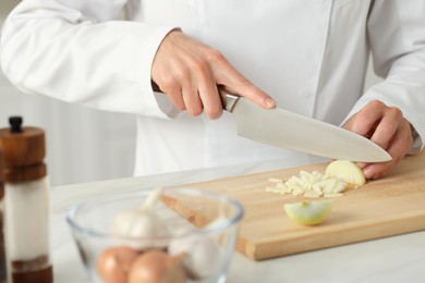 Photo of Professional chef cutting onion at white marble table indoors, closeup