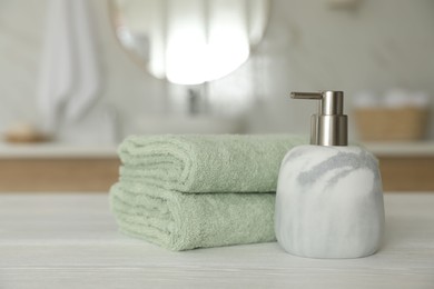 Photo of Clean towels and soap dispenser on white wooden table in bathroom