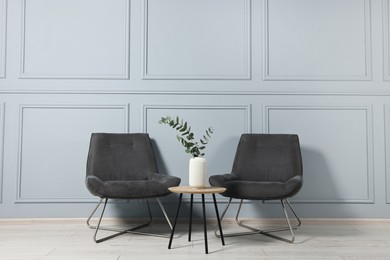 Photo of Comfortable armchairs, side table and eucalyptus indoors