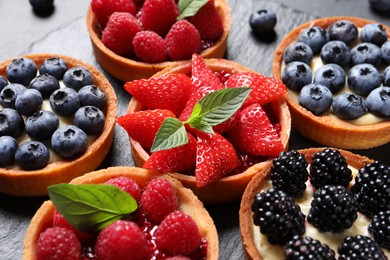 Photo of Tartlets with different fresh berries on slate plate, closeup. Delicious dessert