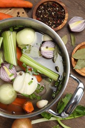 Photo of Pot and different ingredients for cooking tasty bouillon on wooden table, flat lay