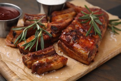 Photo of Tasty roasted pork ribs served with sauce and rosemary on wooden table, closeup