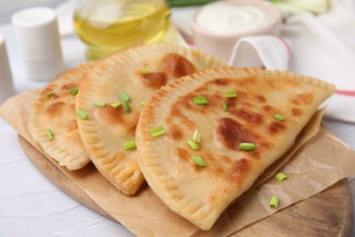 Delicious fried chebureki with cheese and green onion on white textured table
