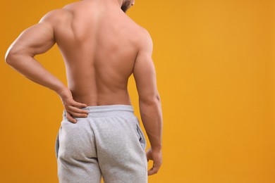 Photo of Man suffering from back pain on orange background, back view. Space for text