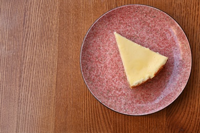 Plate with slice of cheesecake on wooden table, top view