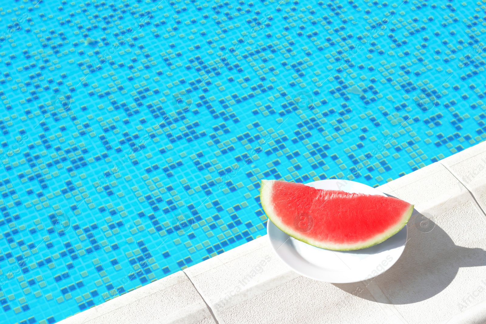 Photo of Slice of fresh juicy watermelon on white plate near swimming pool outdoors. Space for text