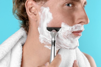 Handsome young man shaving on color background