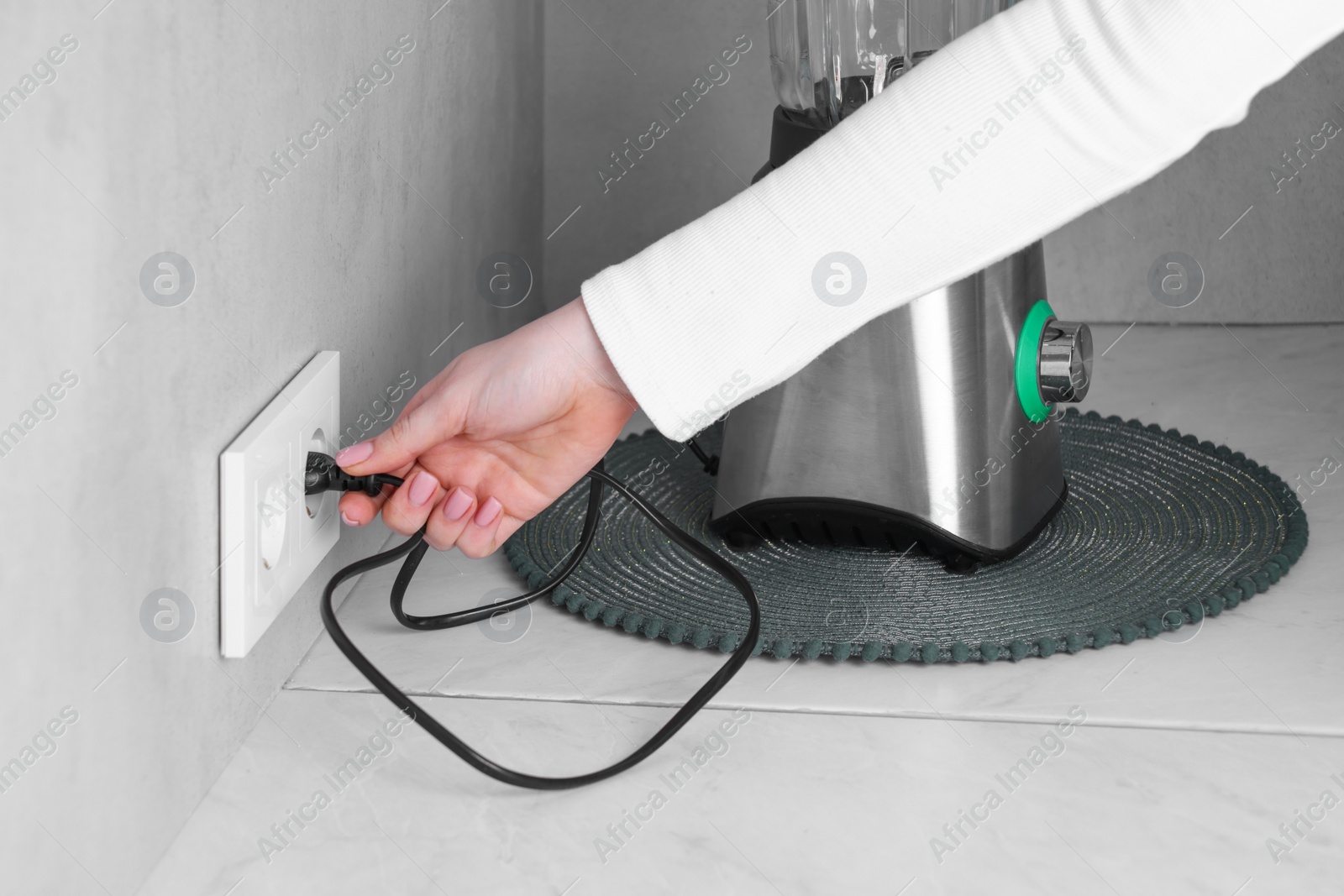 Photo of Woman plugging blender into socket at white table indoors, closeup