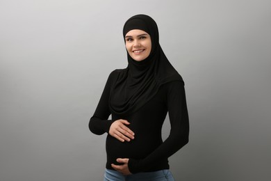 Portrait of pregnant Muslim woman in hijab on light gray background