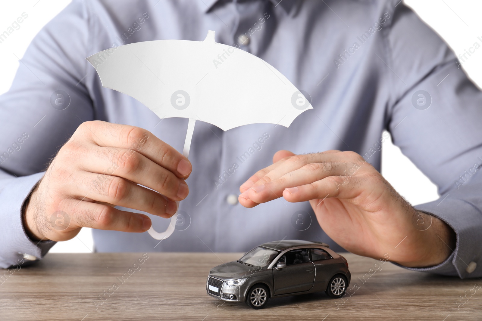 Photo of Male insurance agent covering toy car with paper cutout umbrella and hand at table, closeup