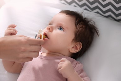 Photo of Mother giving pacifier to her little baby on bed, closeup