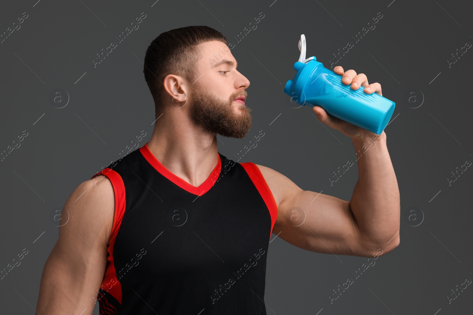 Photo of Young man with muscular body holding shaker of protein on grey background