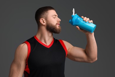 Young man with muscular body holding shaker of protein on grey background