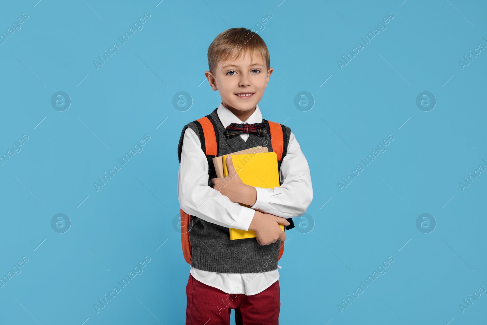 Photo of Happy schoolboy with backpack and books on light blue background