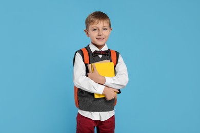 Happy schoolboy with backpack and books on light blue background