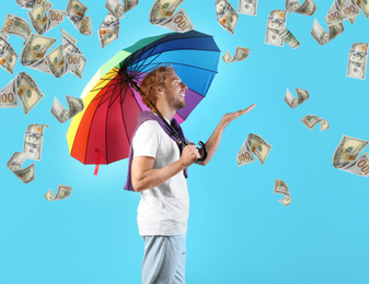 Man with rainbow umbrella under money rain on color background 