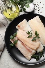 Plate with raw cod fish, parsley, oil and spices on light textured table, flat lay