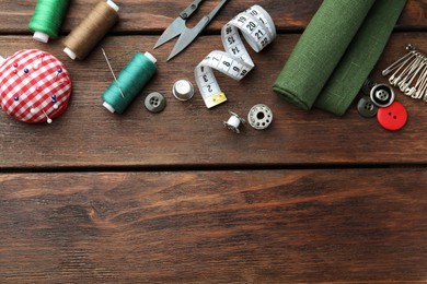 Threads and other sewing supplies on wooden table, flat lay. Space for text