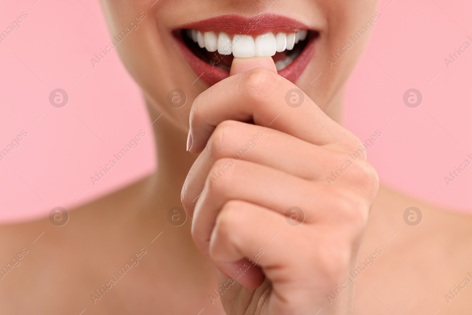 Photo of Woman with beautiful lips biting her finger on pink background, closeup