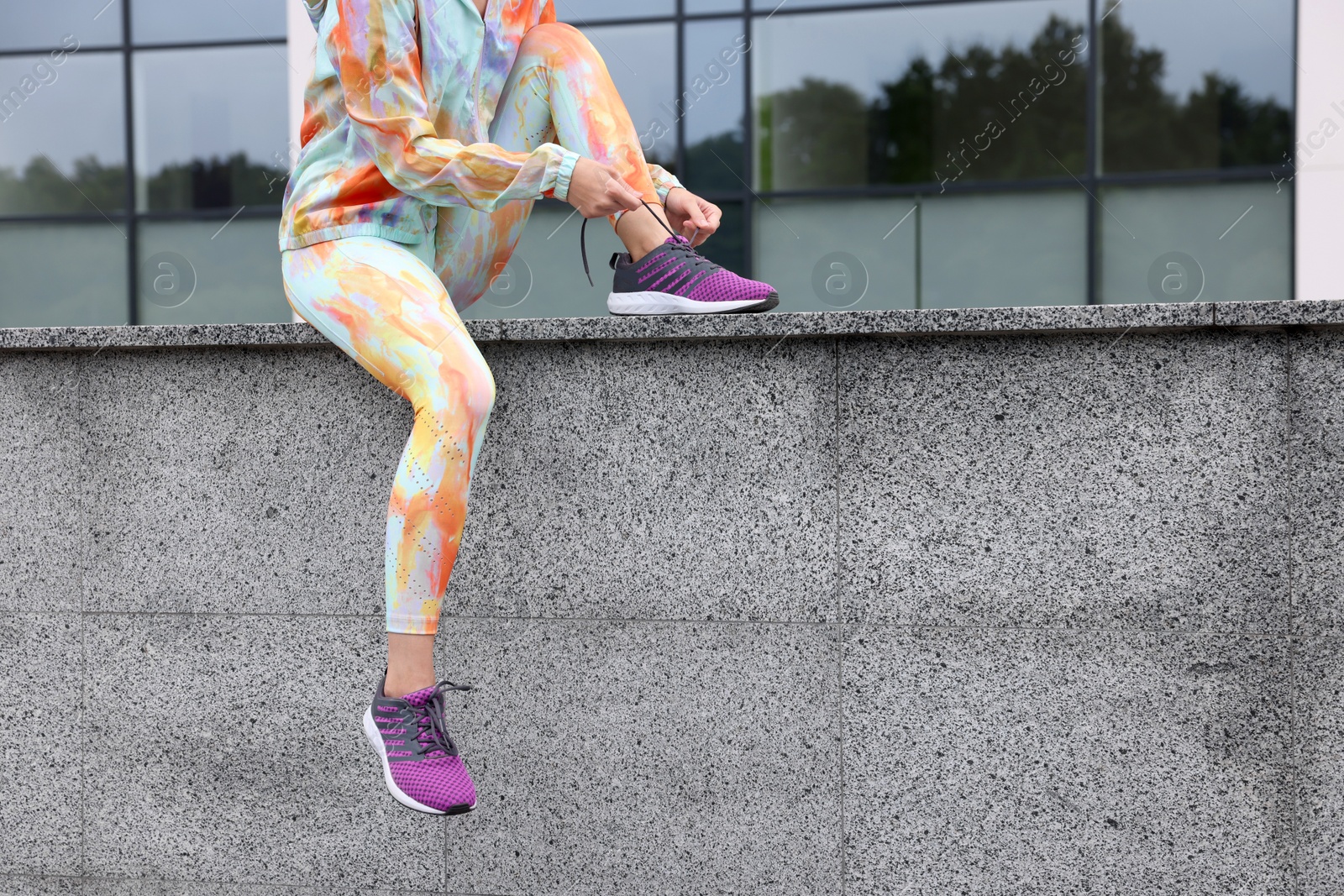 Photo of Woman in gym clothes tying shoelace of sneakers on street, closeup. Space for text