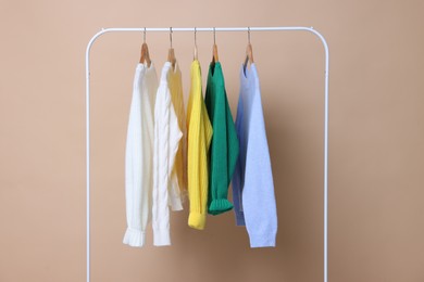 Photo of Rack with different warm sweaters on beige background