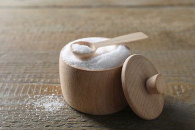 Organic salt in bowl and spoon on wooden table, closeup