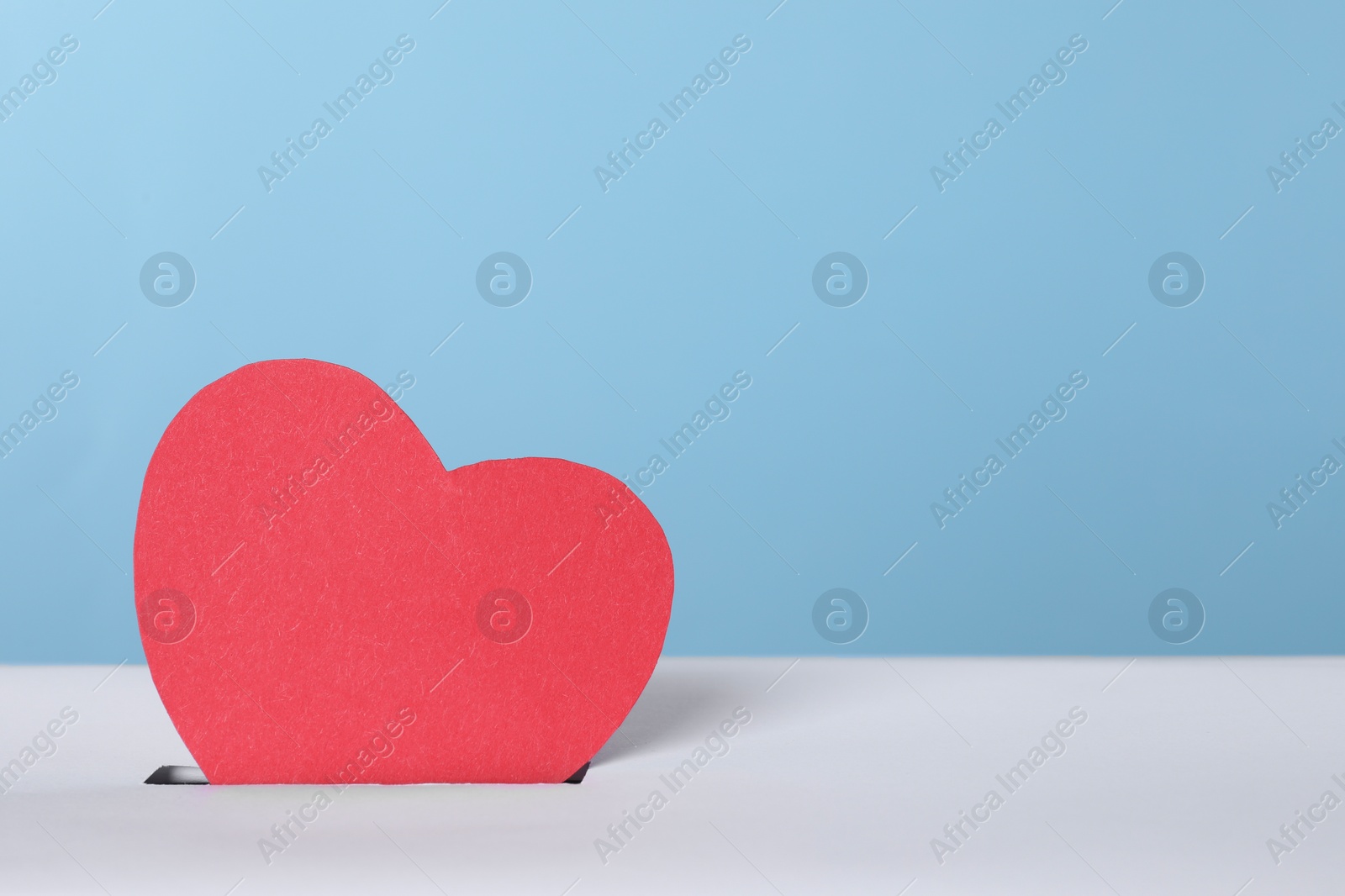 Photo of Red heart into slot of donation box against light blue background, space for text