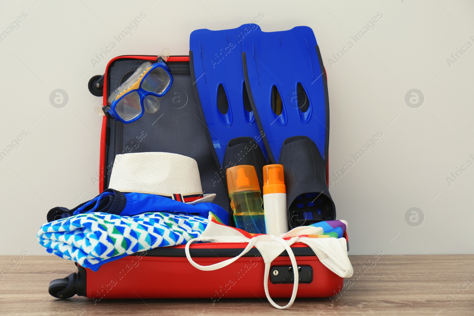Photo of Open suitcase with clothing and swimming accessories on table