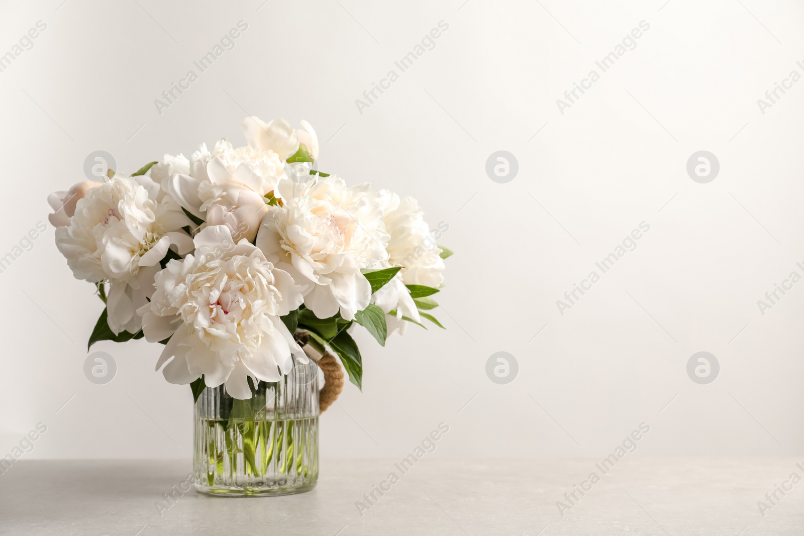 Photo of Vase with beautiful blooming peonies on table against light background