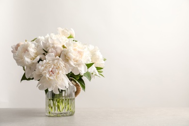 Vase with beautiful blooming peonies on table against light background